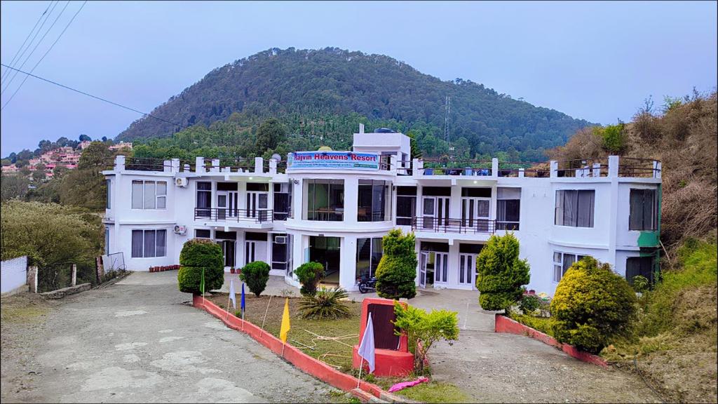 a large white building with a mountain in the background at Rajvin Heavens Resort in Bhīm Tāl