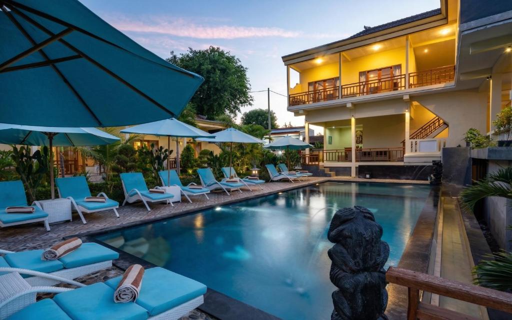 a pool with chairs and umbrellas next to a building at Bali Nusa Cottage in Nusa Lembongan