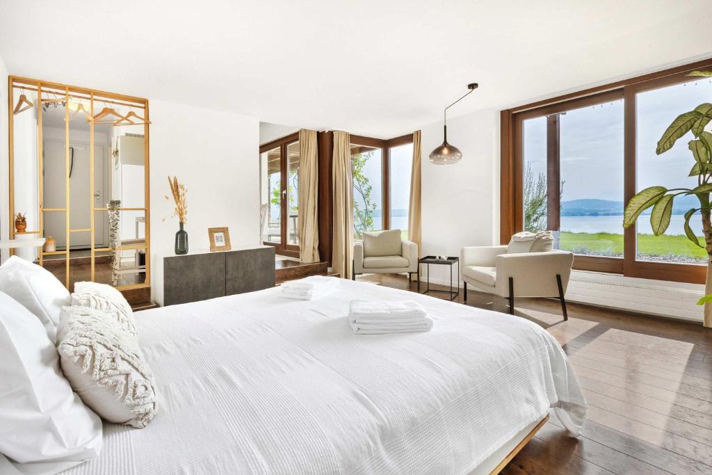 a white bedroom with a large white bed and windows at Studio with panoramic view in Bellerive