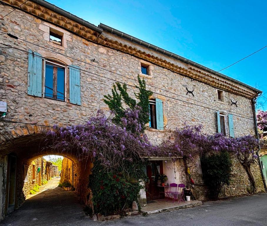 an old brick building with purple flowers on it at Longo maï in Vallon-Pont-dʼArc