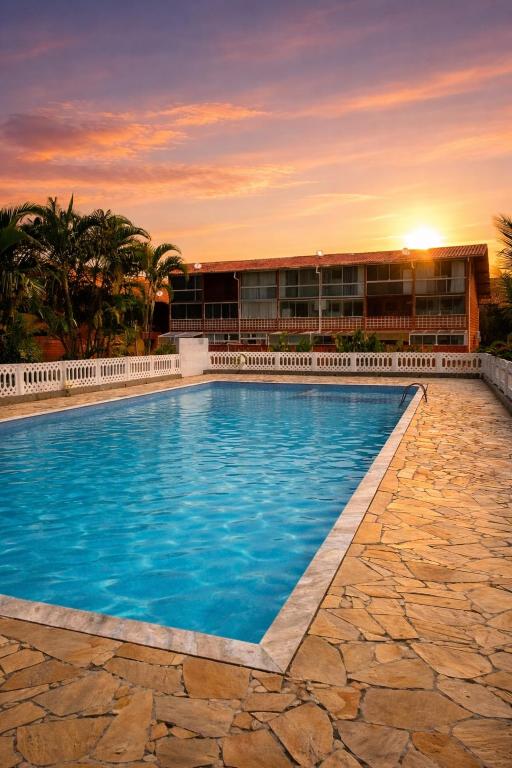 a swimming pool in front of a building with a sunset at Chalé Maresia Maranduba in Maranduba