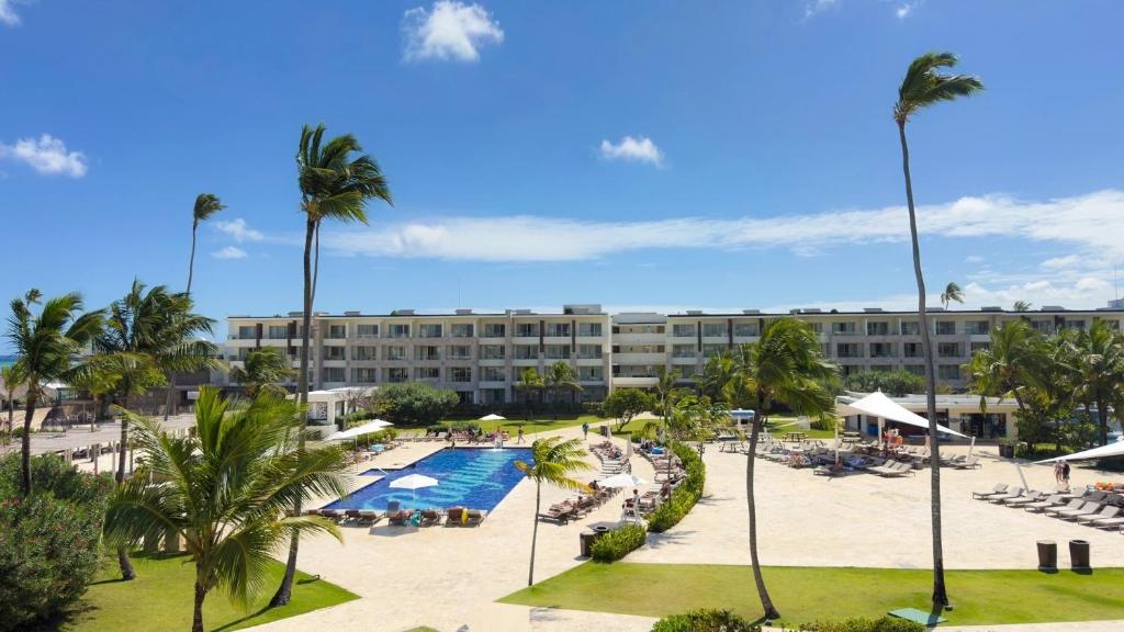 Resort pool deck with blue swimming pool, palm trees, loungers, and hotel building.