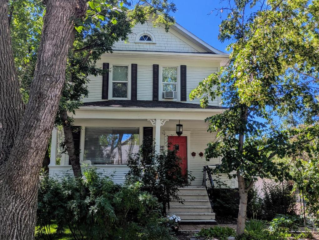 a white house with a red door and trees at Charles Street Vacation Home in Lethbridge