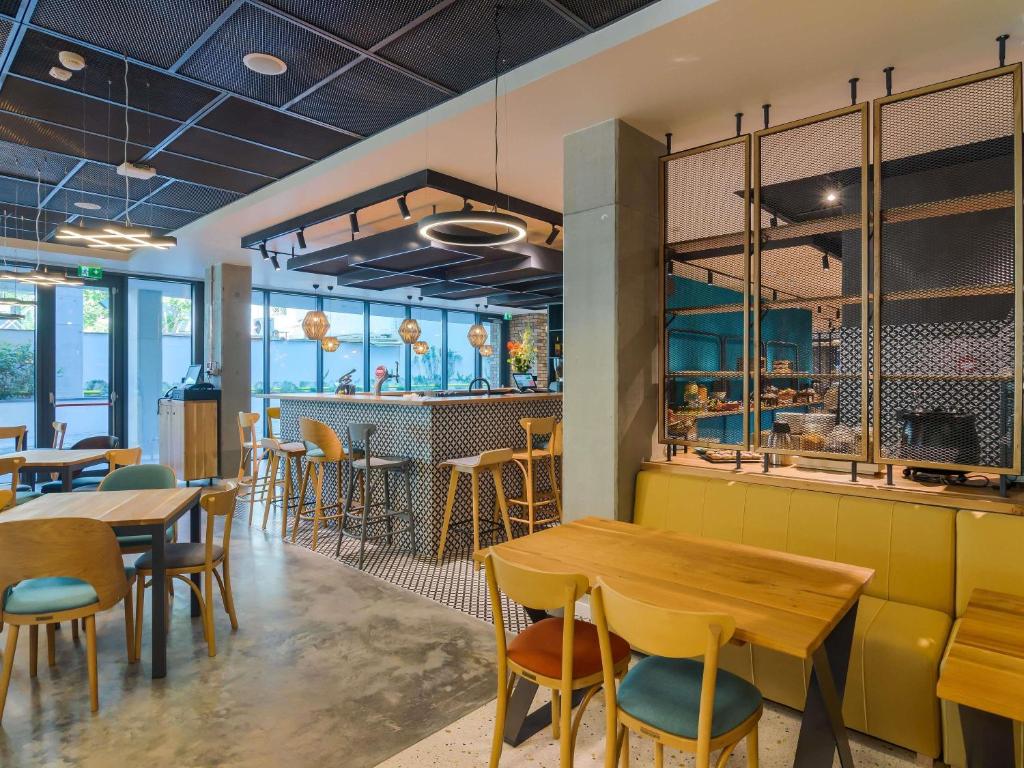 Hotel dining area with wooden tables, patterned tile floor, bar with high stools, pastry counter and backlit glass display at ibis Styles Bucharest City Center in Bucharest