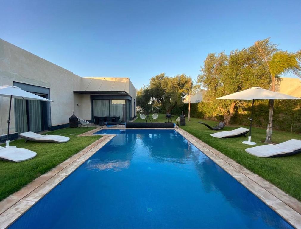 a swimming pool in a yard with chairs and umbrellas at Villa nomad marrakech in Douar bel Rhanodour