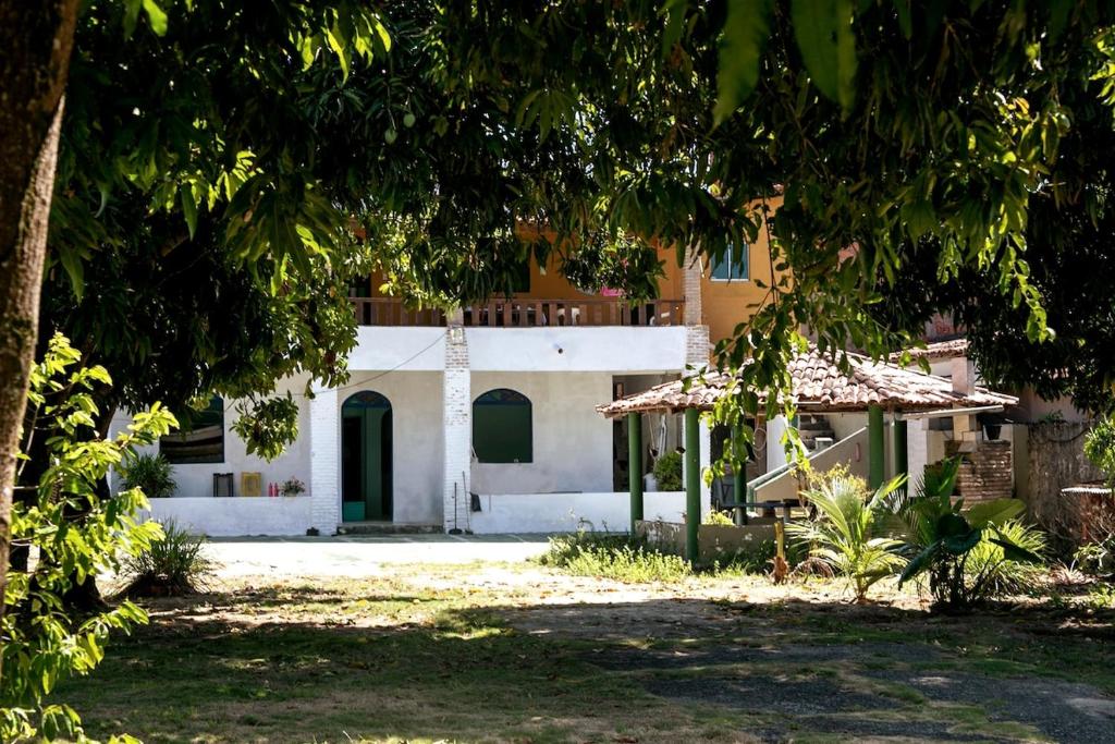 a white house with a tree in front of it at Berlinque Pet Friendly - Muito espaço perto do mar in Vera Cruz de Itaparica