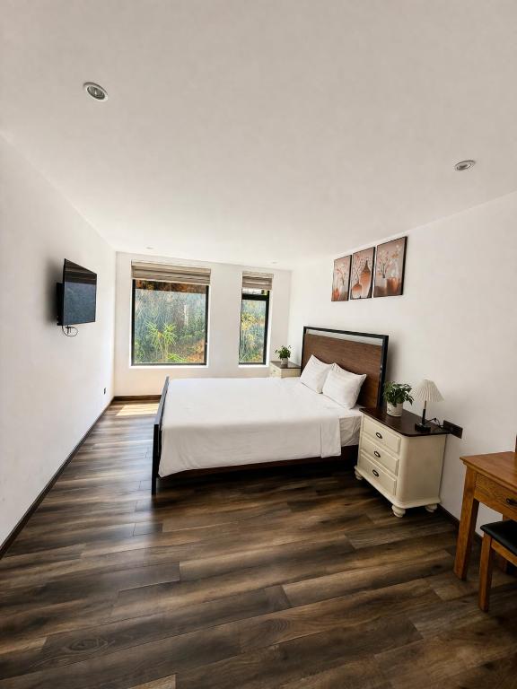 a bedroom with a bed and a desk and two windows at Camly Resort DaLat in Ấp Ða Lợi