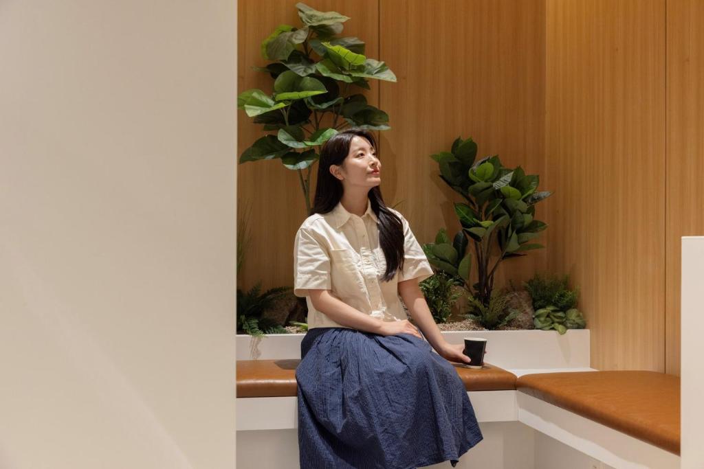 a woman sitting on a bench in front of plants at Daejeon Anook Hotel Yuseong Oncheon Station in Daejeon