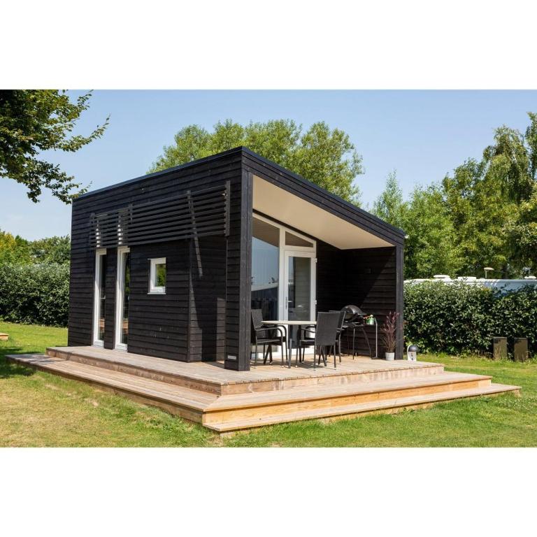 a small black tiny house with a deck at DCU-Camping Åbyskov Strand in Åbyskov