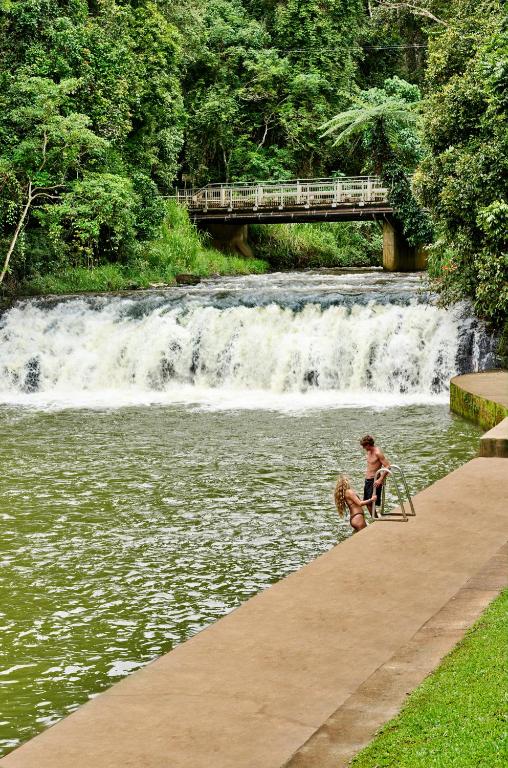a man and a woman sitting on a bench near a waterfall at Malanda Falls Retreat in Malanda