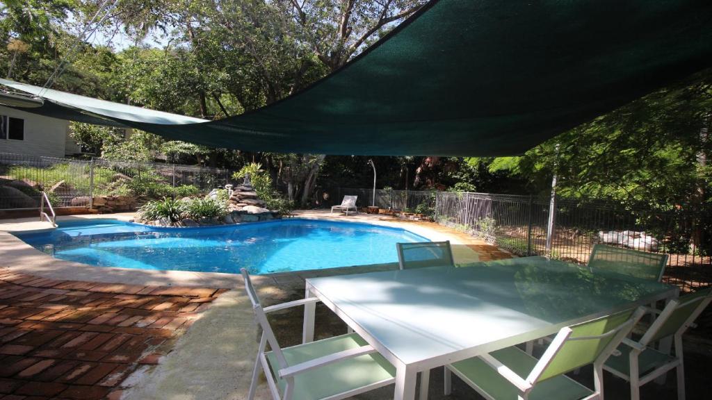 a pool with a table and chairs under a green umbrella at Del Haven Holiday House in Arcadia
