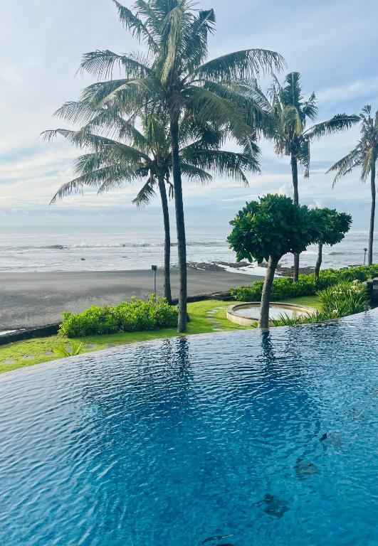 a swimming pool next to a beach with palm trees at Anapuri Villas in Ketewel