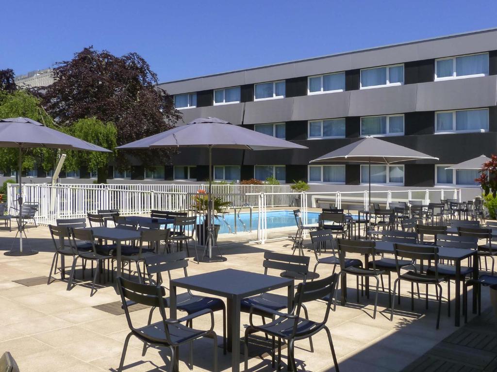 a group of tables and chairs with umbrellas next to a building at Novotel Caen Côte de Nacre in Caen