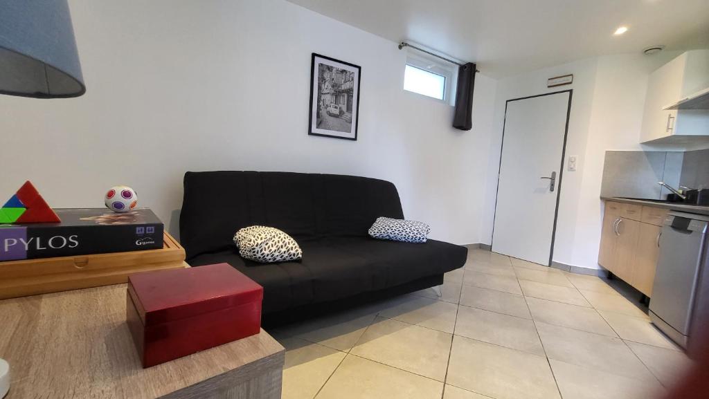a living room with a black couch and a kitchen at studio Les merles à Saint-Égrève in Saint-Égrève