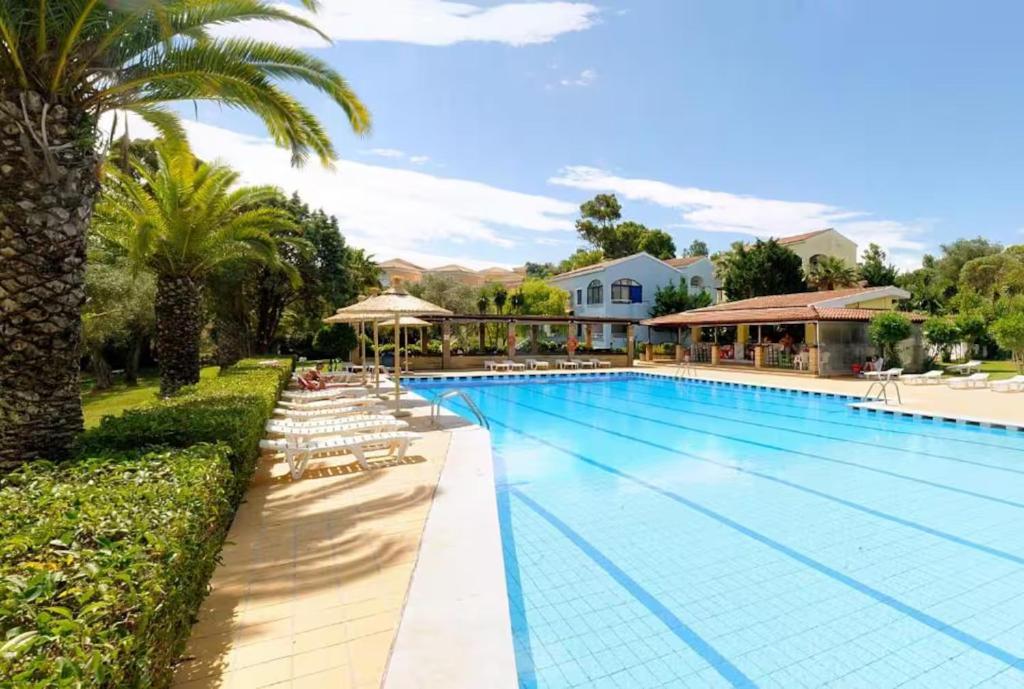 a large swimming pool with chairs and palm trees at The Garden Maisonette in Gouvia