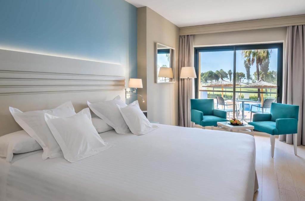 a bedroom with a large white bed with two blue chairs at Barceló Costa Ballena Golf & Spa in Costa Ballena