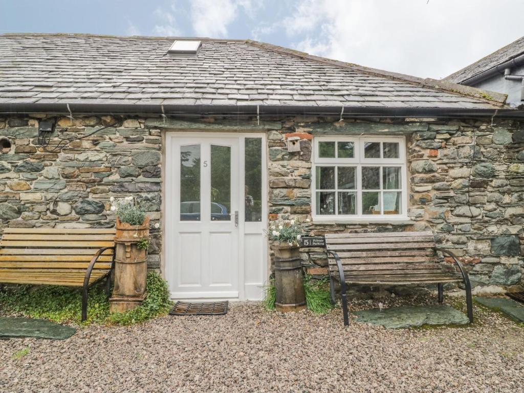 a stone cottage with a white door and two benches at Mews Cottage 5 in Keswick