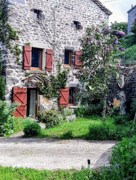 an old stone house with red shuttered windows at Maison ferme équestre du Ténéré in Saint-Jean-Lachalm