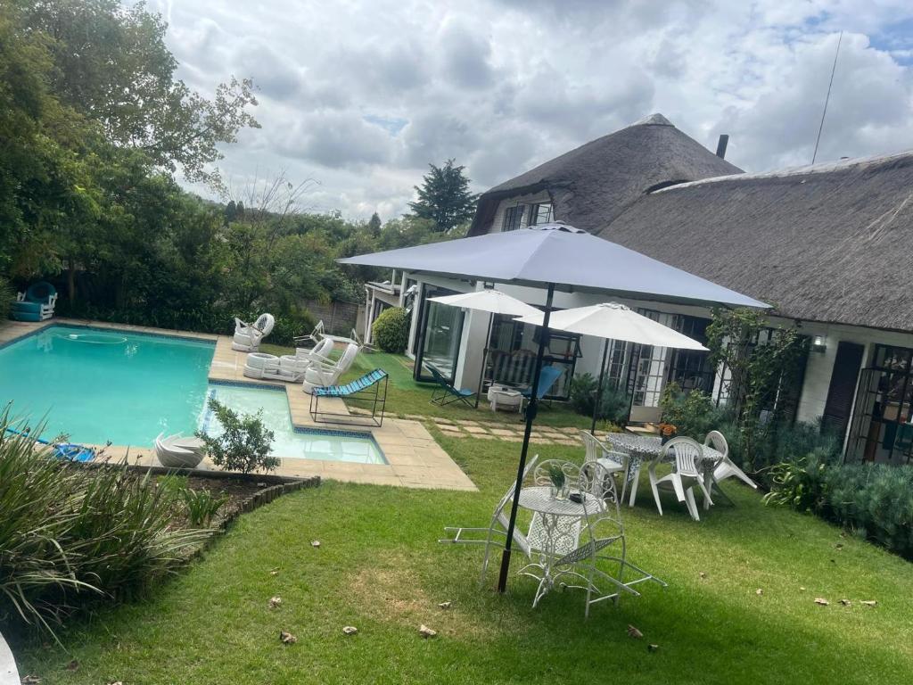 a house with an umbrella and chairs and a pool at Muco Guest House in Johannesburg