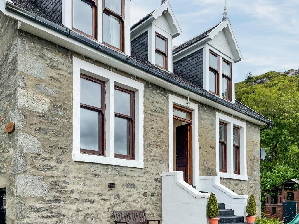 a stone house with white windows and a mountain at Aldersyde in Tighnabruaich