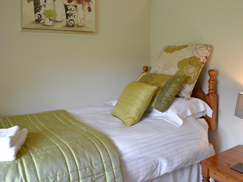 a bed with green and white sheets and pillows at Clematis Cottage in Burnsall