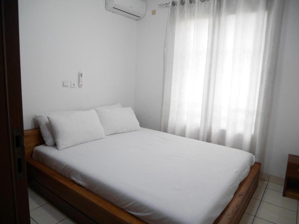 a bed with white sheets in a room with a window at LA MAISON SEONE f4 FAMILLE in Abidjan