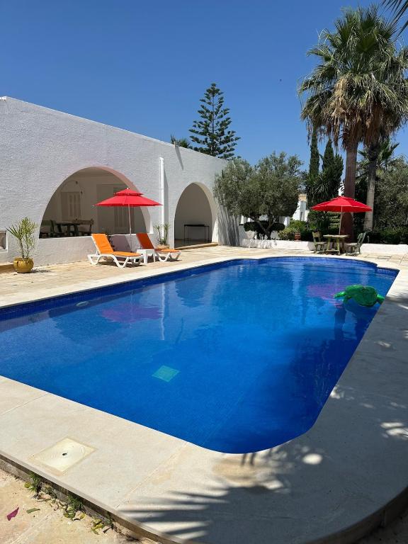a large blue swimming pool with two chairs and umbrellas at La Baïa Cozy in Sukrah