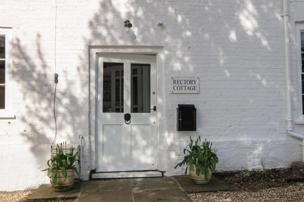 a white building with a door and two potted plants at Rectory Cottage in Alton