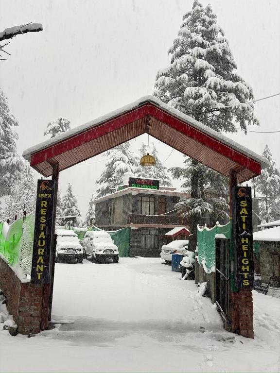 a snow covered gate to a building with cars parked at Sati Heights in Vashisht