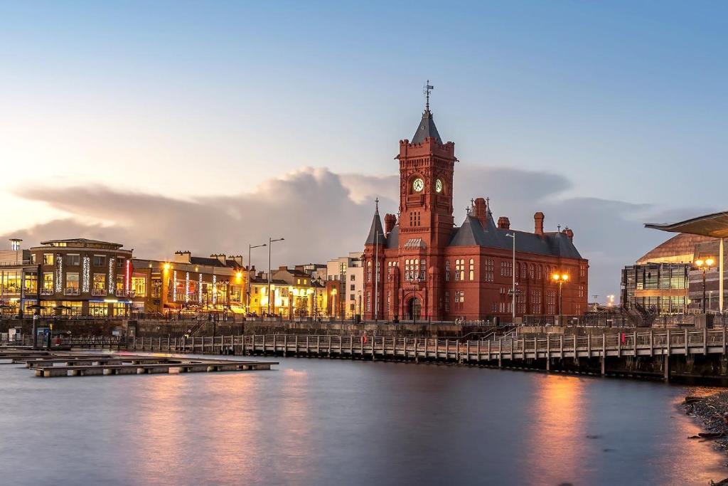 a large building with a clock tower and a river at Principality Apartment in Cardiff