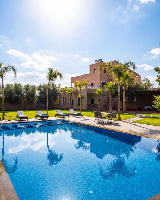 a swimming pool with palm trees and a building at Blumen Villa in Marrakesh