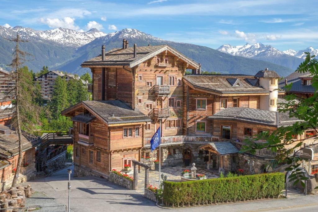 a large wooden house with mountains in the background at Hostellerie du Pas de l'Ours "Relais et Châteaux" in Crans-Montana