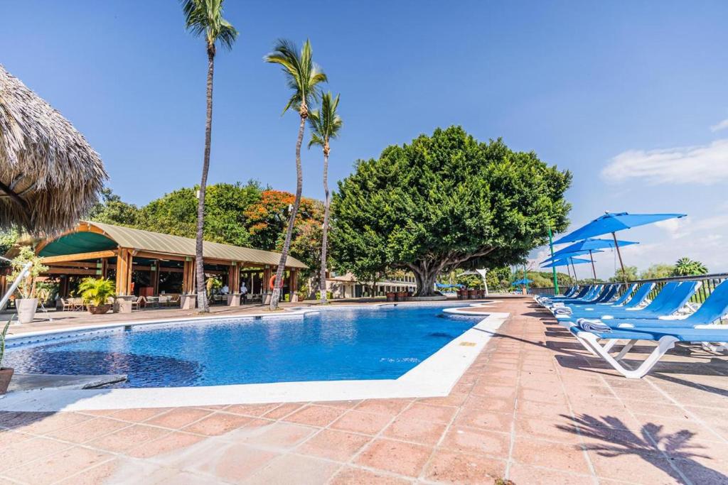 een zwembad bij een resort met blauwe ligstoelen en palmbomen bij Real de Chapala in Ajijic