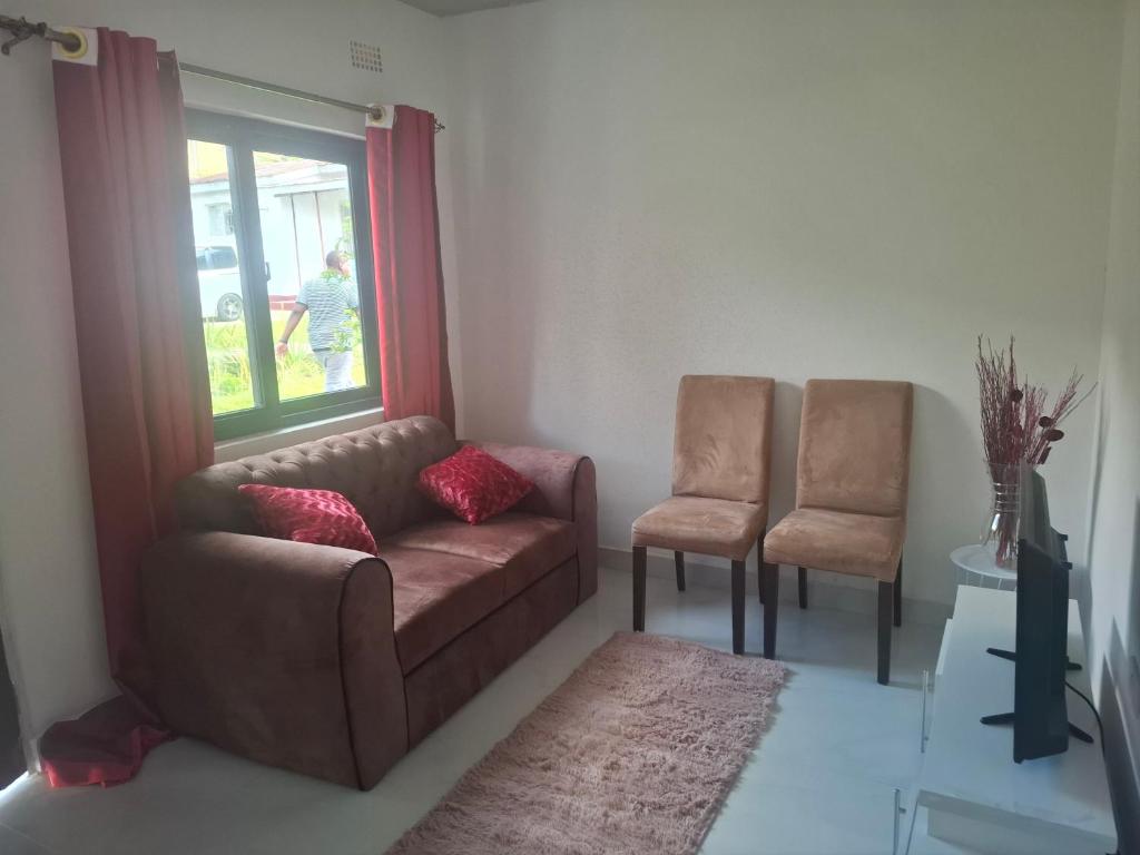a living room with a couch and two chairs at Rose's Garden Cottages in Lusaka