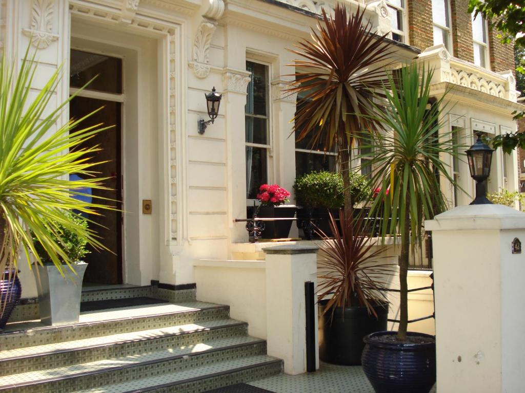 uma casa branca com vasos de plantas nos degraus em London Visitors Hotel em Londres