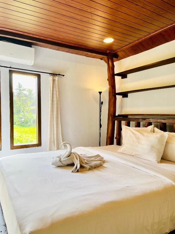 a bedroom with a white bed with a wooden ceiling at Sawit House by Natural View in Karangasem