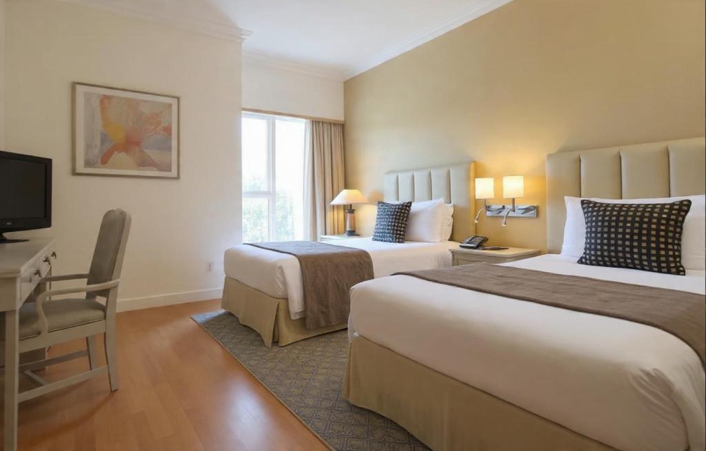 a hotel room with two beds and a desk and a television at Hotel Grand Tela Suite Delhi in Gurgaon