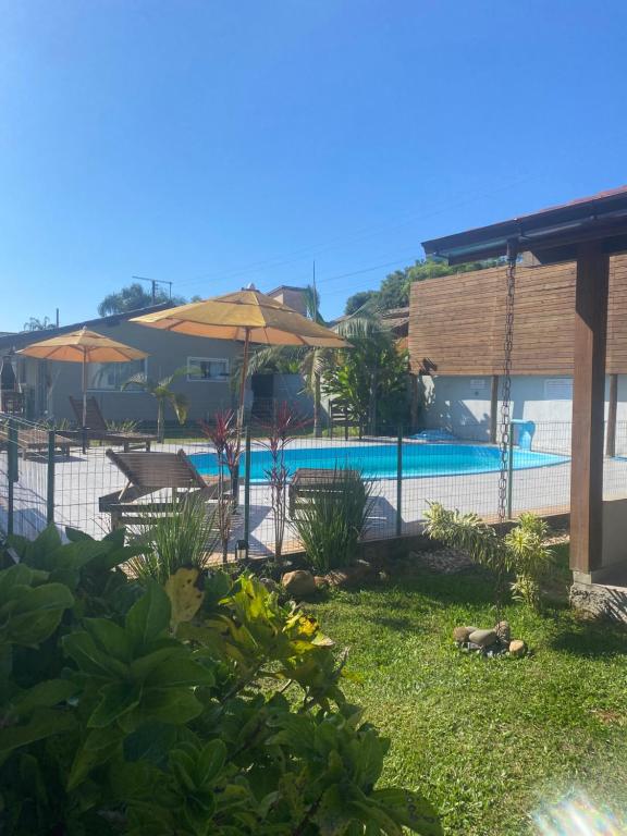a yard with a pool with umbrellas and chairs at Morada Carmem in Praia do Rosa