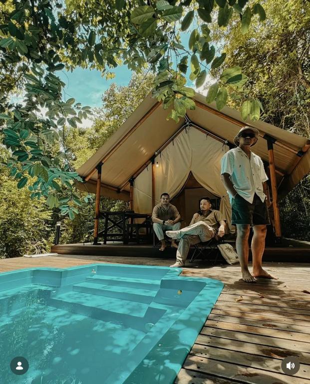 a man standing next to a swimming pool next to a tent at Bandu Buana Glamping in Kuala Pilah