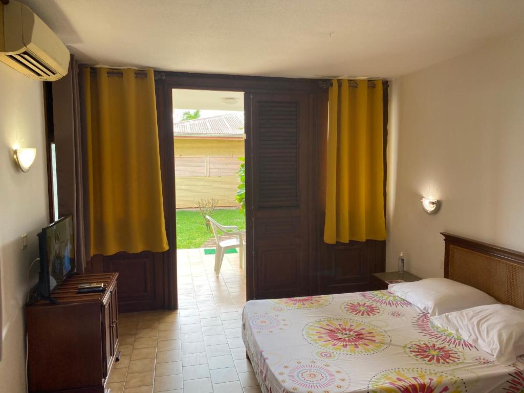 a bedroom with a bed and a door with yellow curtains at Appartement Patronus à 3 min PLAGE POINTE MARIN in Sainte-Anne