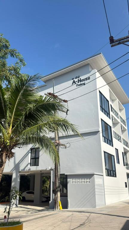 a large white building with a palm tree in front of it at A House Thalang เอ เฮ้าส์ ถลาง in Thalang