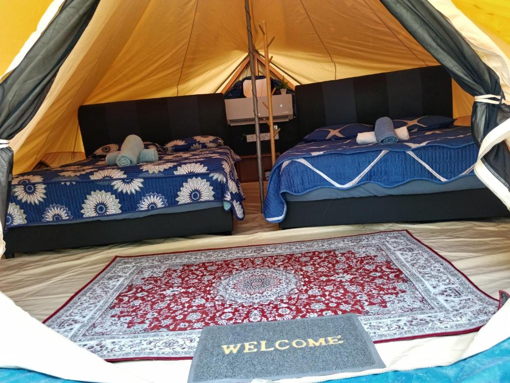 a bedroom with two beds and a welcome mat in a tent at Gaharu glamping park in Jerantut