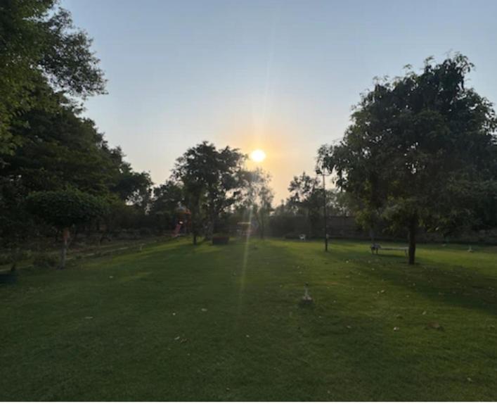 a field with the sun setting in a park at Aaliya Farm House in Dhauj