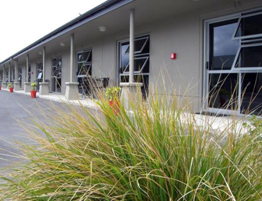 Un bâtiment avec une bande d'herbe haute devant lui dans l'établissement St Johns court motel, à Milton