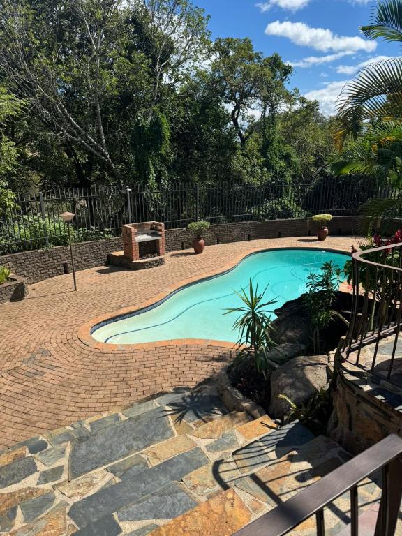 a swimming pool with a brick walkway around it at The Rock & Root Guesthouse Self Catering in Nelspruit