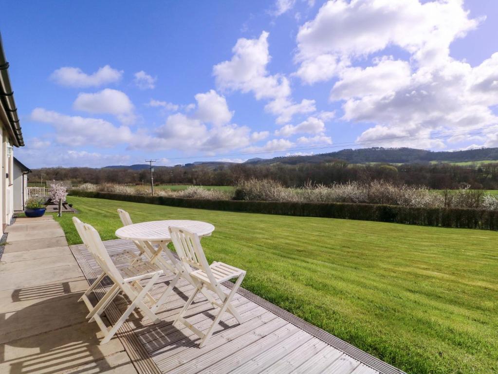 a table and two chairs sitting on a wooden deck with a lawn at Sunny Cottage in Brecon