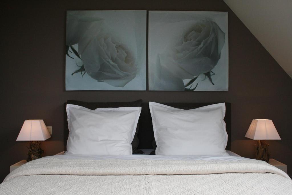 a bedroom with a bed with white pillows and two pictures at B&B Soluna in Oostduinkerke