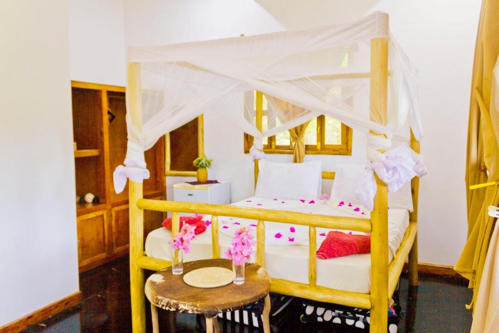 a bedroom with a canopy bed and a table with flowers at Mbao Boutique Bungalows in Jambiani