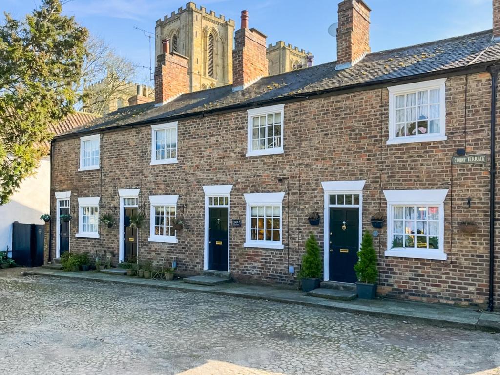 a brick house with white windows and blue doors at Bay Cottage in Ripon