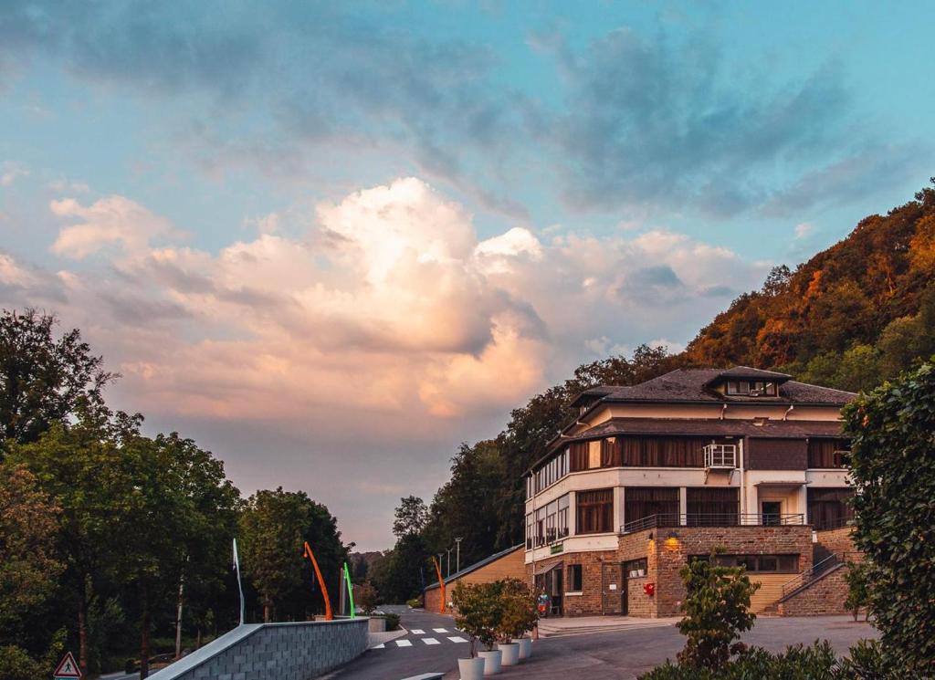 a building in front of a mountain with a cloudy sky at LPM Sporthotel Durbuy in Durbuy